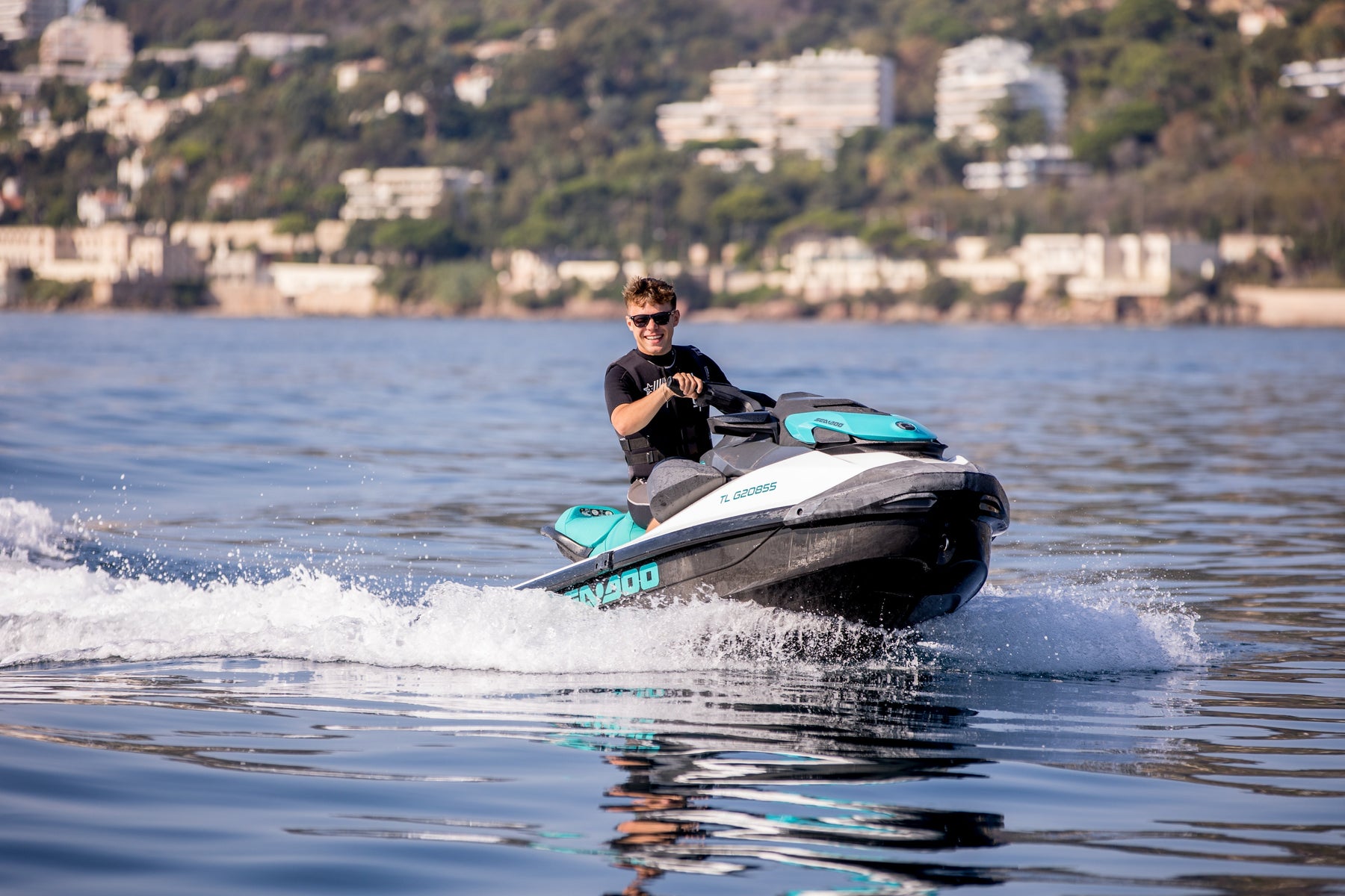 Young man wearing sunglasses and summer clothes riding a jet ski in the sea while smiling 