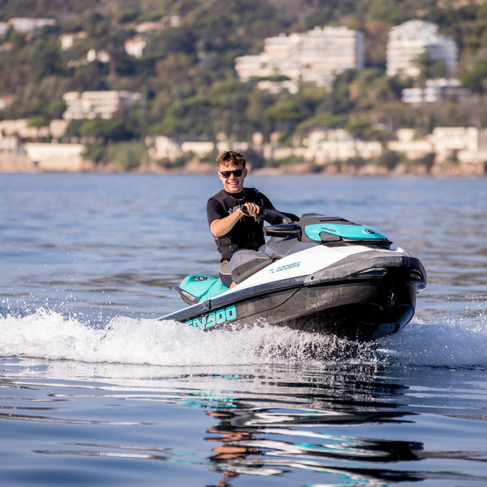 Young man wearing sunglasses and summer clothes riding a jet ski in the sea while smiling 